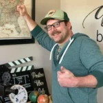 a man in a green hat and glasses holding his thumbs up