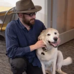a man with a hat and glasses petting a dog